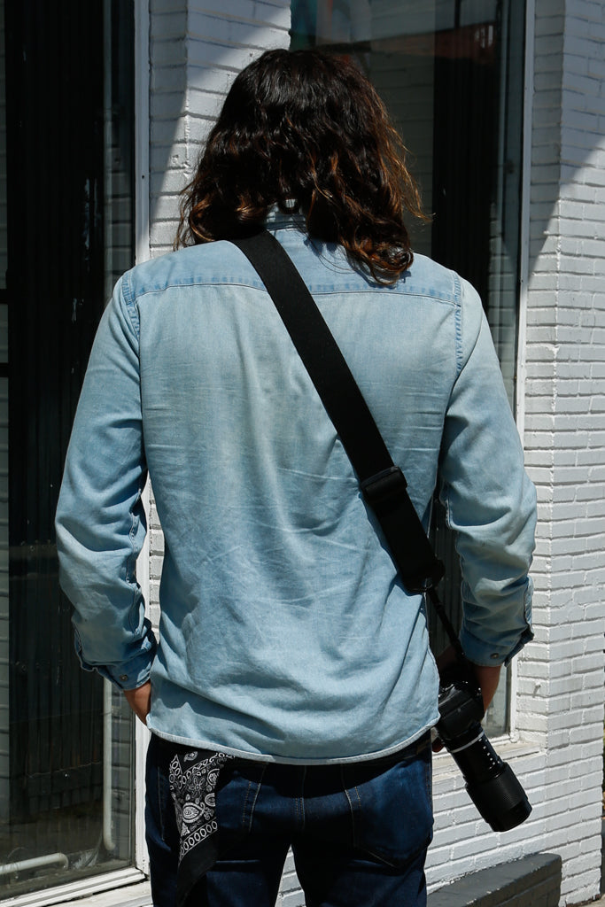 rear view fo a street photographer with a camera strap made of 2" wide heavy-duty elastic material over left shoulder attached to a Sony camera
