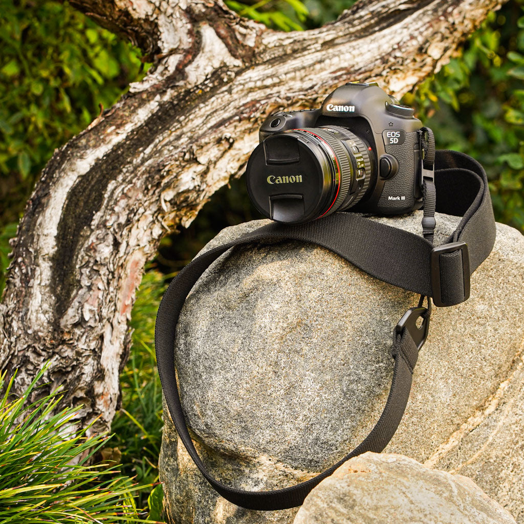 Canon camera on a rock with a camera strap made of 2" wide heavy-duty elastic material attached